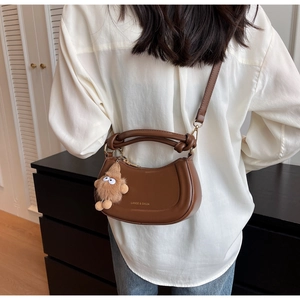 Sac croissant en cuir marron avec poignée nouée et charm peluche porté par un mannequin