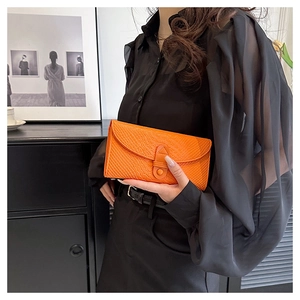 Detail of a bright orange crocodile embossed envelope clutch bag held by a model
