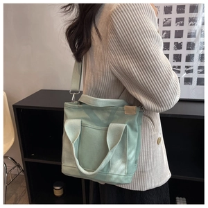 Detail of mint green canvas tote bag with shoulder strap worn by a model in a stylish setting