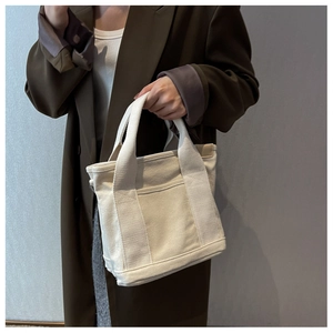 Detail of a beige canvas tote bag with dual handles and front pocket for daily commute