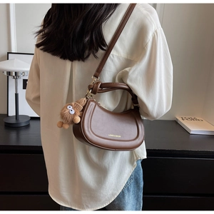 Sac demi-lune en cuir marron avec poignée nouée et breloque monstre en peluche