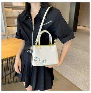 Detail of floral embroidery and green trim on off-white tote bag with gold metal hardware