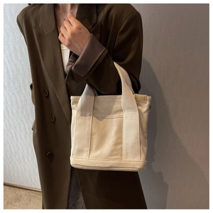 Close-up of off-white canvas tote bag with wide shoulder strap and front storage pocket