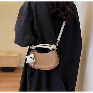 Sac demi-lune marron avec poignée tressée et charm peluche sur un manteau noir