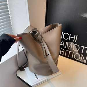 Minimalist beige pebble leather bucket bag with silver hardware on a modern artistic background
