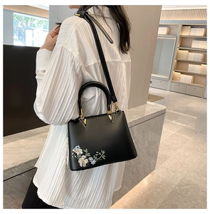 Detailed close-up of a black tote bag with floral embroidery and golden V-shaped metal accents