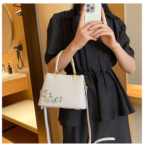 Detailed embroidery on a white crossbody bag featuring floral motifs and gold V-shaped hardware