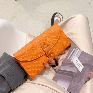 Fashionable bright orange crocodile embossed long flap wallet held in a hand