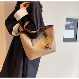 Detail view of khaki large tote bag with brown straps and tassel charm on black coat