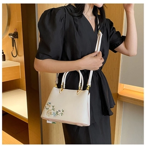 Detail of floral embroidery on cream crossbody bag held by a model in a warm interior