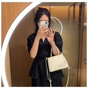 Detailed embroidery on white faux leather handbag with green trim and V-gold hardware