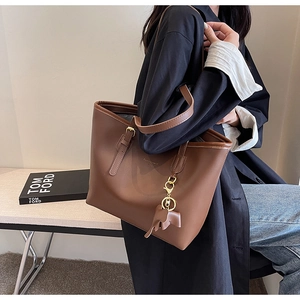 Detail of large brown leather tote bag with elephant pendant and dual shoulder straps
