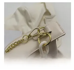 Detail shot of elegant golden metal hooks and white acrylic chain on cream cloud bag