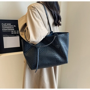 Detailed close-up of a black woven tote bag texture worn with a stylish beige trench coat