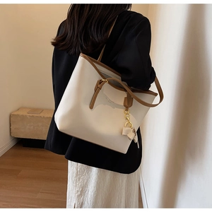 Detail of a large cream tote bag with brown trim and bow charm worn by a model