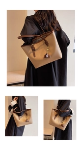 Close-up of a beige tote bag with brown straps, fashion lettering and bow charm detail