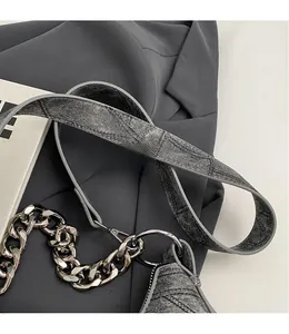 Detail of denim crossbody bag featuring a metal chain strap and smooth adjustable textile strap