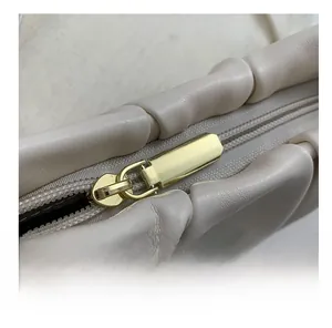 Detail of smooth gold zipper and pleated cream leather on stylish cloud bag