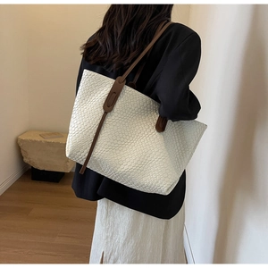 Close-up detail of white woven tote bag with brown leather handles in indoor setting