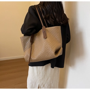 Close-up of a khaki woven tote bag with crossbody strap on a model in a black blazer