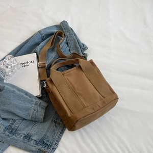 Brown canvas tote bag with adjustable shoulder strap on blue denim jacket background