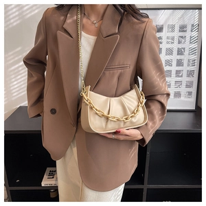 Detail of beige pleated cloud bag with chunky gold chain strap worn over a brown blazer