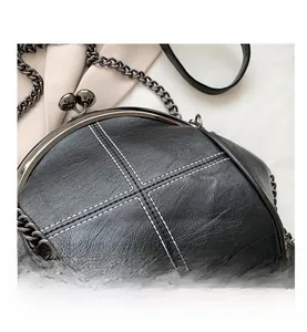 Detail shot of black leather shell bag with white cross stitching and metal clasp closure