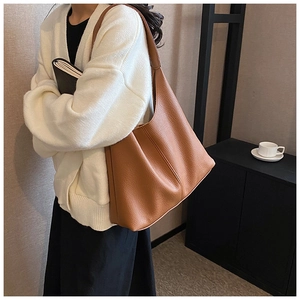 Detail of a large brown pebbled leather tote bag worn on shoulder in a minimalist room