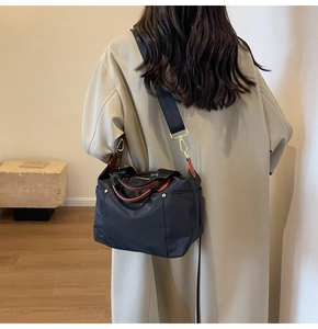 Detail of navy nylon tote bag with leather handles shown as a crossbody on a model
