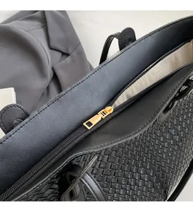 Close-up of woven leather texture on black tote bag with gold zipper and herringbone lining
