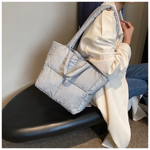 Close-up of a silver quilted puffer tote bag with a glitter finish and wide shoulder strap