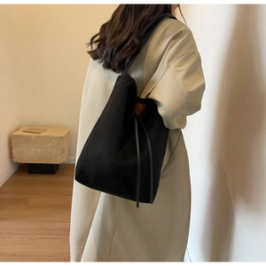 Detailed side view of a large black suede tote bag styled with a minimalist beige trench coat