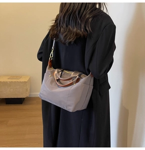 Detailed view of grey nylon shoulder bag with brown leather straps and gold metal zippers