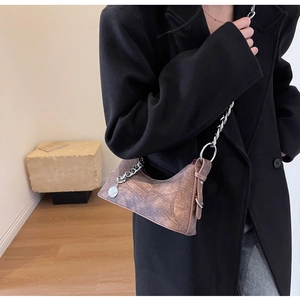 Detail of vintage brown leather textured chain bag shown on a model in black wool coat