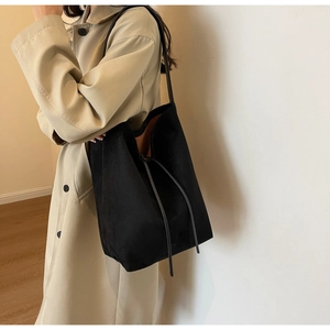 Detail of black suede bucket bag featuring chic knot strap and orange interior lining