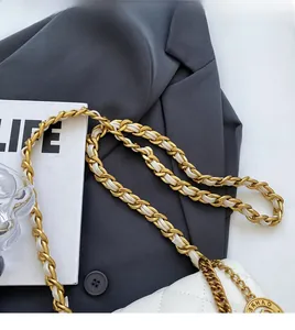 Detail of white quilted crossbody bag with golden chain strap and round metal logo charm