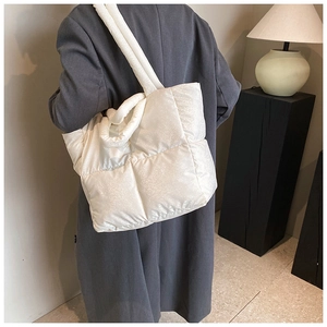 Detailed view of white quilted puffer tote bag with wide padded shoulder strap shown on model