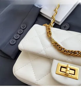 Detail of white quilted crossbody bag with gold chain strap and metal turn-lock closure