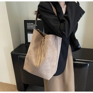 Close-up of beige suede tote bag with drawstring detail worn by a model in black suit