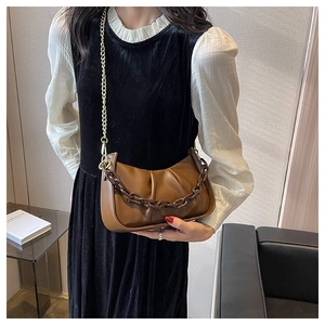Detail of a brown ruched cloud bag featuring gold metal and resin chain shoulder straps