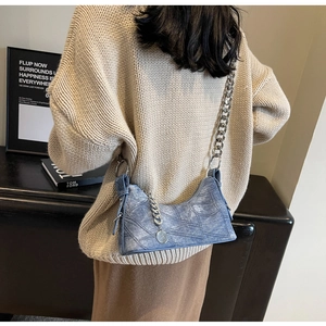 Blue washed denim crescent bag with silver chunky chain strap on a beige sweater