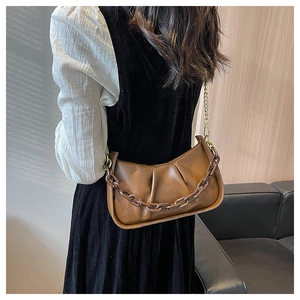 Detail view of brown pleated cloud bag with stylish gold chain strap on a model