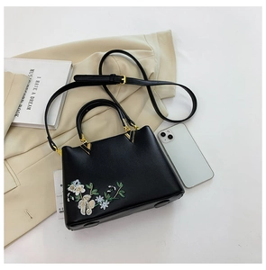 Detail of black tote bag with floral embroidery, dual handles and gold metal hardware