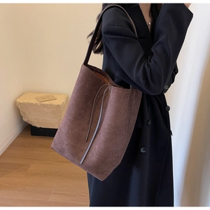 Close-up of a large dark brown suede tote bag showing its soft texture and side straps