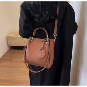 Brown litchi texture bucket bag with adjustable strap worn by a model in a home setting