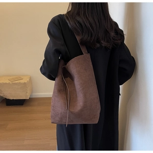 Brown suede tote bag shown on shoulder with long drawstrings and retro minimalist design
