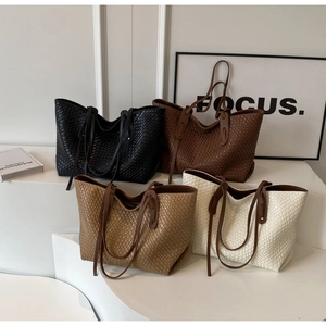 Detailed view of large woven tote bags in four neutral colors on a modern display stand