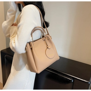 Detail of beige lychee pattern leather handbag with fashion charm worn by model