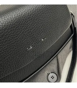 Gros plan sur la texture cuir noir grainé et le logo argenté imprimé sur ce sac bandoulière
