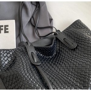 Close-up detail of the intricate black woven leather texture on the large tote bag